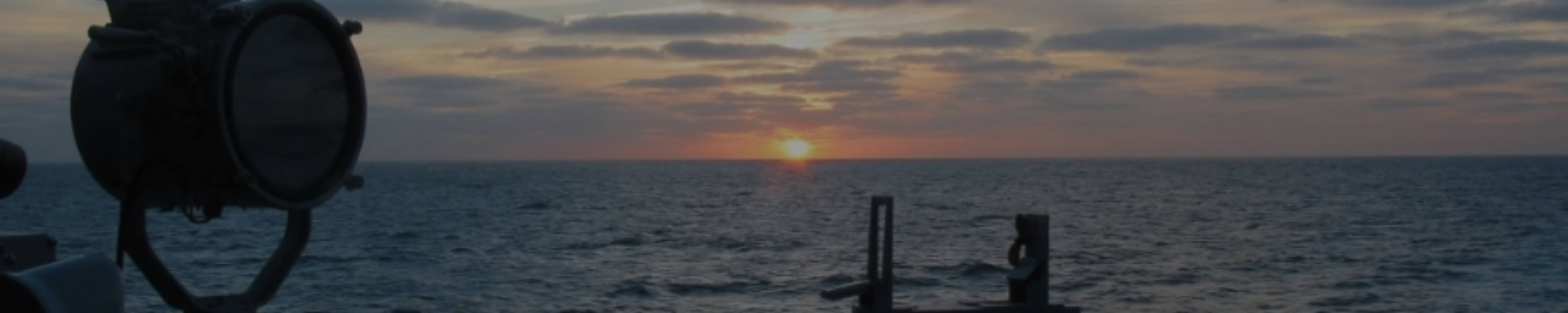 Zonsondergang boven de zee, gezien vanaf een M-Fregat met kompas en seinlamp op de voorgrond.